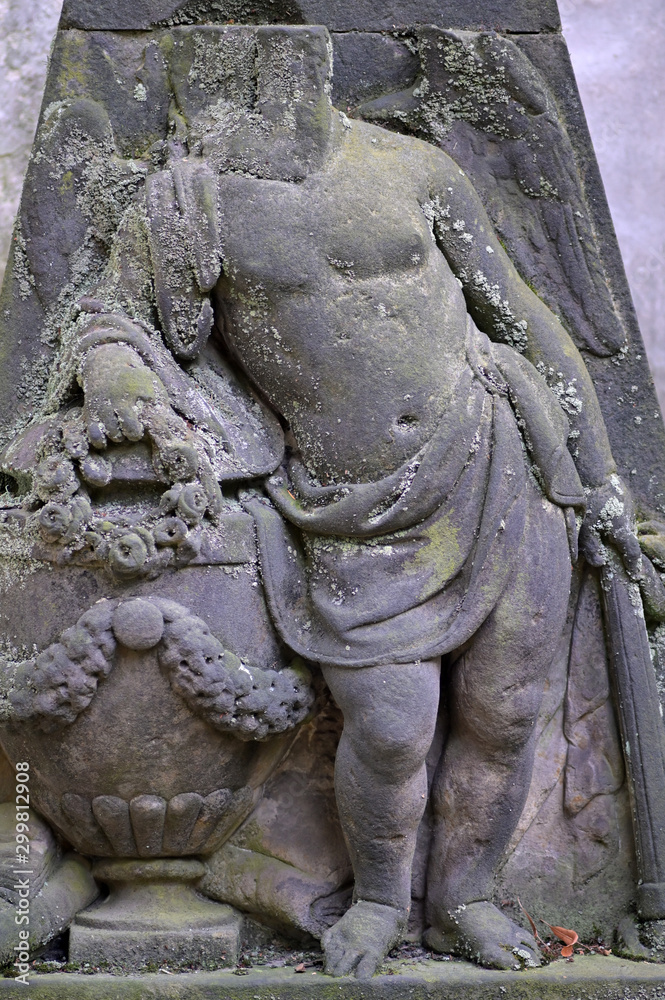 A headless and moss covered sandstone sculpture of an angel in front of a crypt.