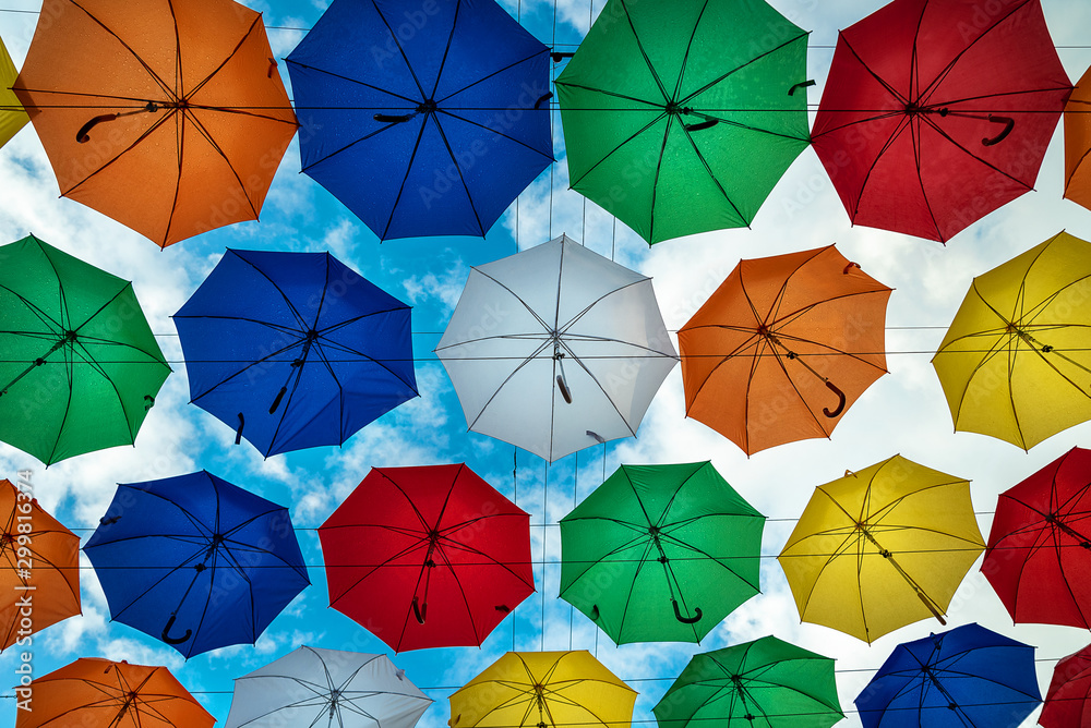 Naklejka premium Multicolored umbrellas against a cloudy sky hanging on ropes handles in the bottom