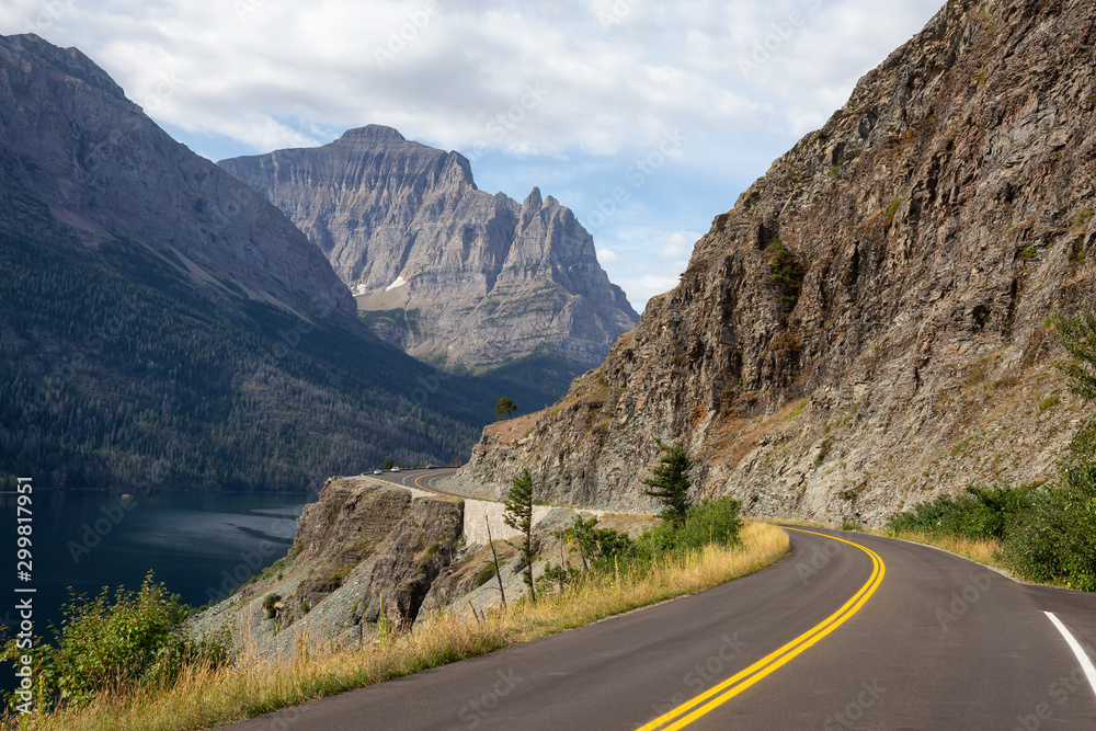 Beautiful View of Scenic Highway with American Rocky Mountain Landscape in the background during a Cloudy Summer Morning. Taken in Glacier National Park, Montana, United States.