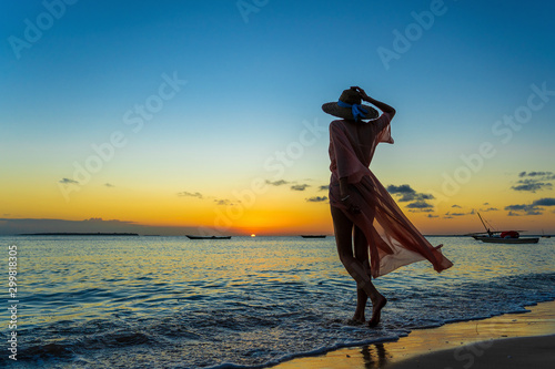 Beautiful girl in a straw hat and pareo on the beach during sunset of Zanzibar island, Tanzania, east Africa