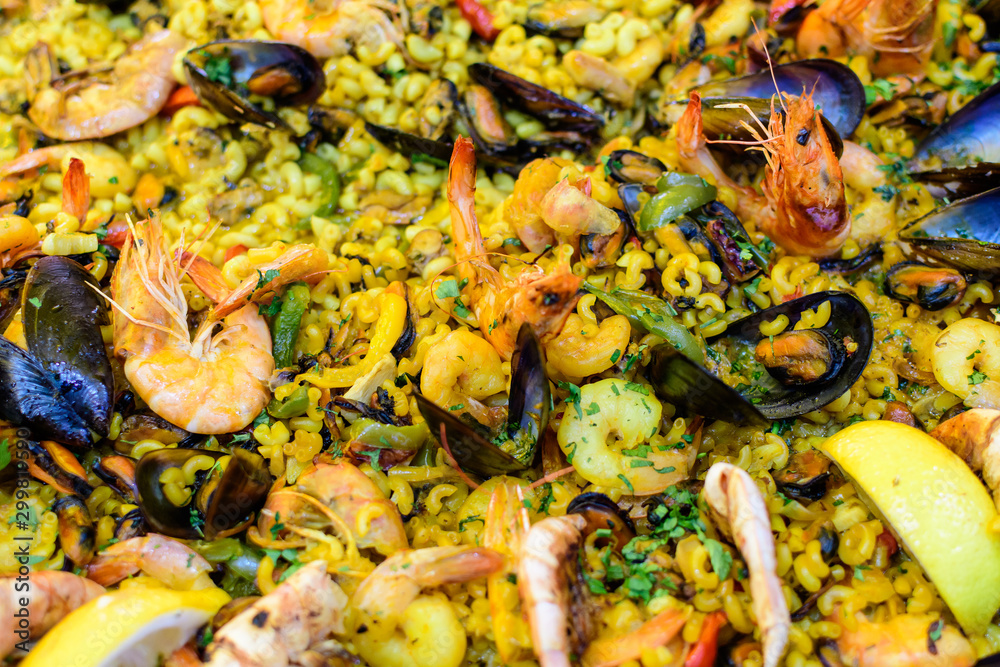 Close up of large portion of traditional Spanish paella dish freshly being cooked with seafood and pasta in a frying pan at a street food festival, ready to eat seafood, side view, selective focus Close up of large portion of traditional Spanish paella dish freshly being cooked with seafood and pasta in a frying pan at a street food festival, ready to eat seafood, side view, selective focus