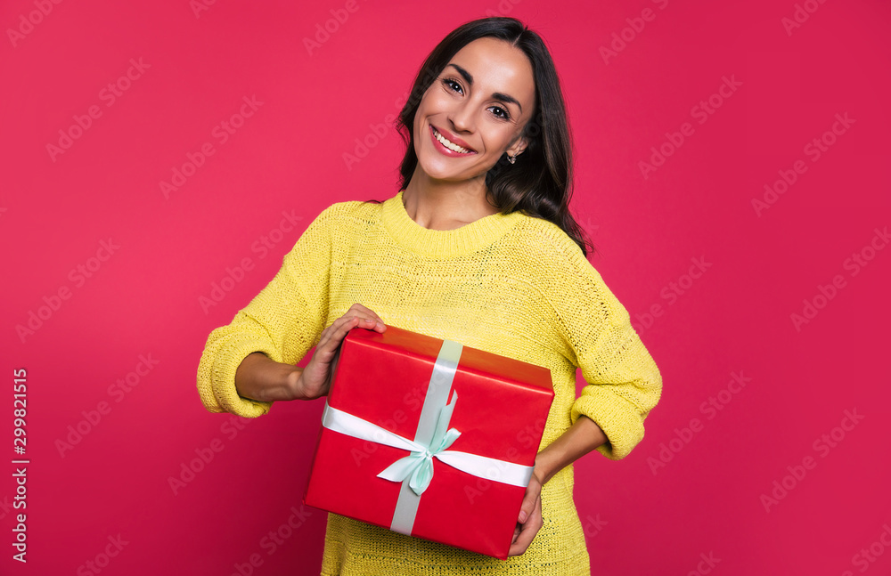 Gift time. Stunning girl in a yellow knitted sweater is posing with a big red box with a blue ribbon in her hands, looking at the camera and smiling charmingly. Gift time. Stunning girl in a yellow knitted sweater is posing with a big red box with a blue ribbon in her hands, looking at the camera and smiling charmingly.
