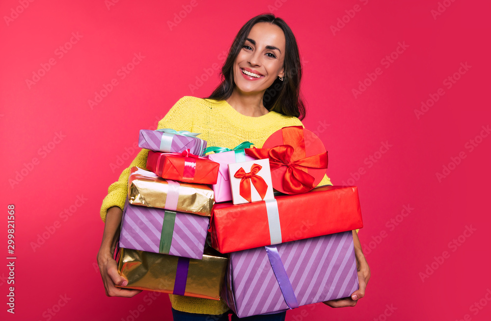 A bunch of happiness. Attractive dark-haired woman is looking happily at the camera, holding a great amount of multicolored present boxes in her hands. A bunch of happiness. Attractive dark-haired woman is looking happily at the camera, holding a great amount of multicolored present boxes in her hands.