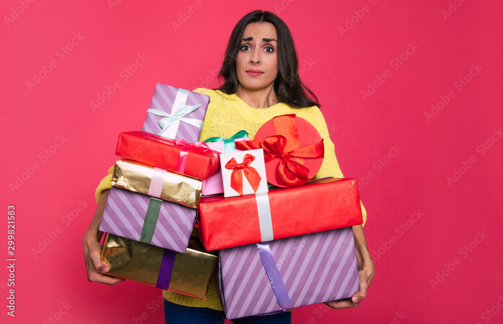So happy that it is heavy. Confused young girl is holding a several amount of multicolored presents in her hands, looking at the camera with surprise. So happy that it is heavy. Confused young girl is holding a several amount of multicolored presents in her hands, looking at the camera with surprise.