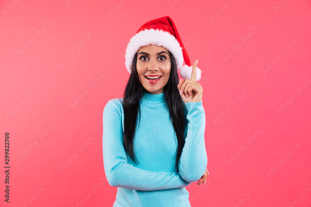 I’ve got an idea! Beautiful girl in a red Christmas hat and blue sweater and in a red hat is standing with her right index finger pointing in the air and laughing. I’ve got an idea! Beautiful girl in a red Christmas hat and blue sweater and in a red hat is standing with her right index finger pointing in the air and laughing.