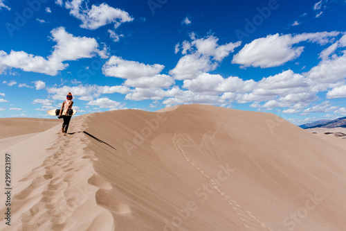 Woman walking up a dune with a sand board