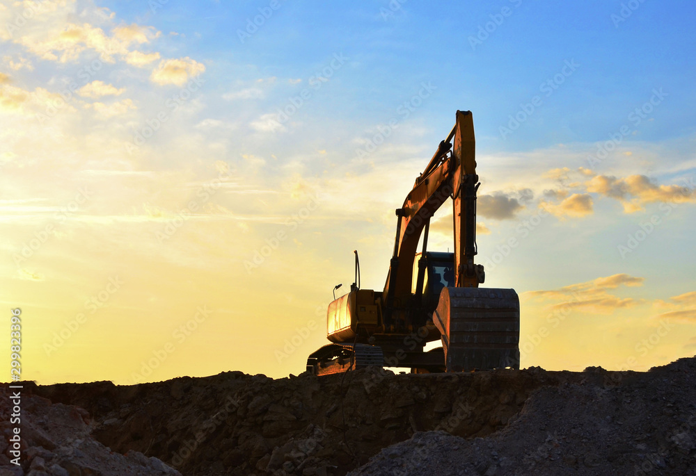 Heavy excavator working at construction site on a background  sunset. Crushing and processing of rocks in the mining quarry.  Special heavy construction equipment for road construction