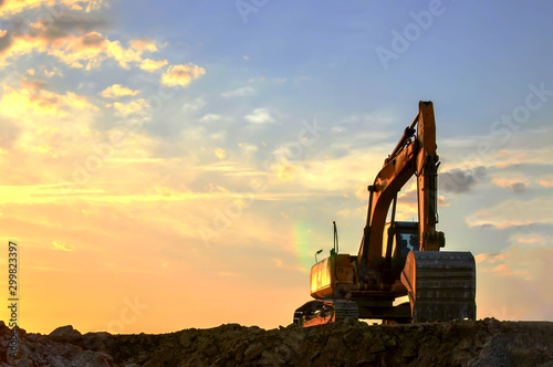 Heavy excavator working at construction site on a background sunset. Crushing and processing of rocks in the mining quarry. Special heavy construction equipment for road construction