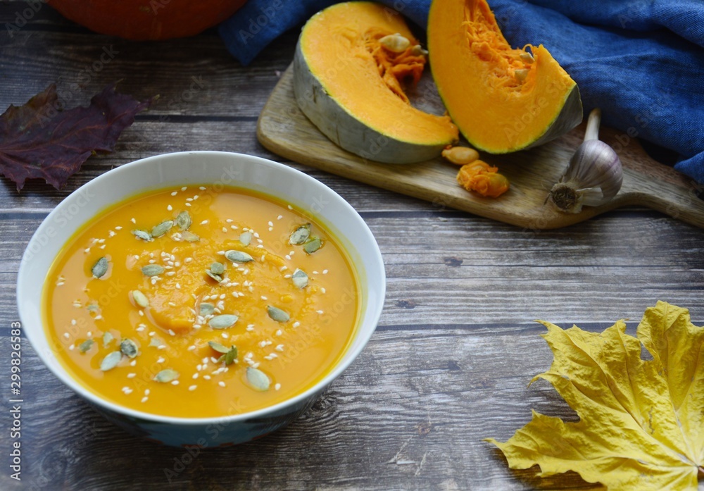 pumpkin soup in a deep plate, slices of pumpkin on a cutting board and yellow maple leaf on a gray wooden background with space for text. f pumpkin soup in a deep plate, slices of pumpkin on a cutting board and yellow maple leaf on a gray wooden background with space for text. f