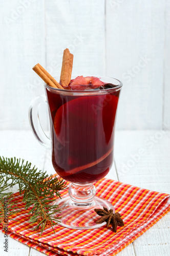 Hot mulled wine in a glass on a white wooden background. A traditional warming winter wine drink with aromatic spices. Vertical view.