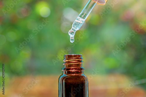 Spa beauty concept. Herbal essential massage oil dripping into bottle. Pipette with essence drop and bottle, closeup on blurred nature background. Selective focus