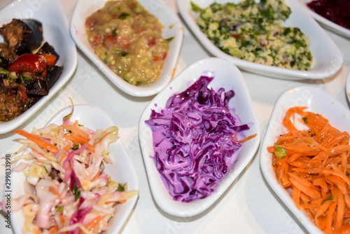 A set of different salads served on plates on a white tablecloth.