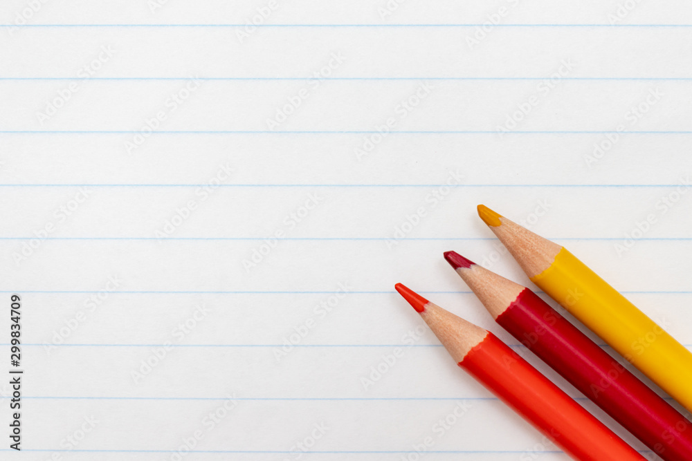 Colorful pencils on the background of a white lined sheet of notebook close-up with copy space Colorful pencils on the background of a white lined sheet of notebook close-up with copy space