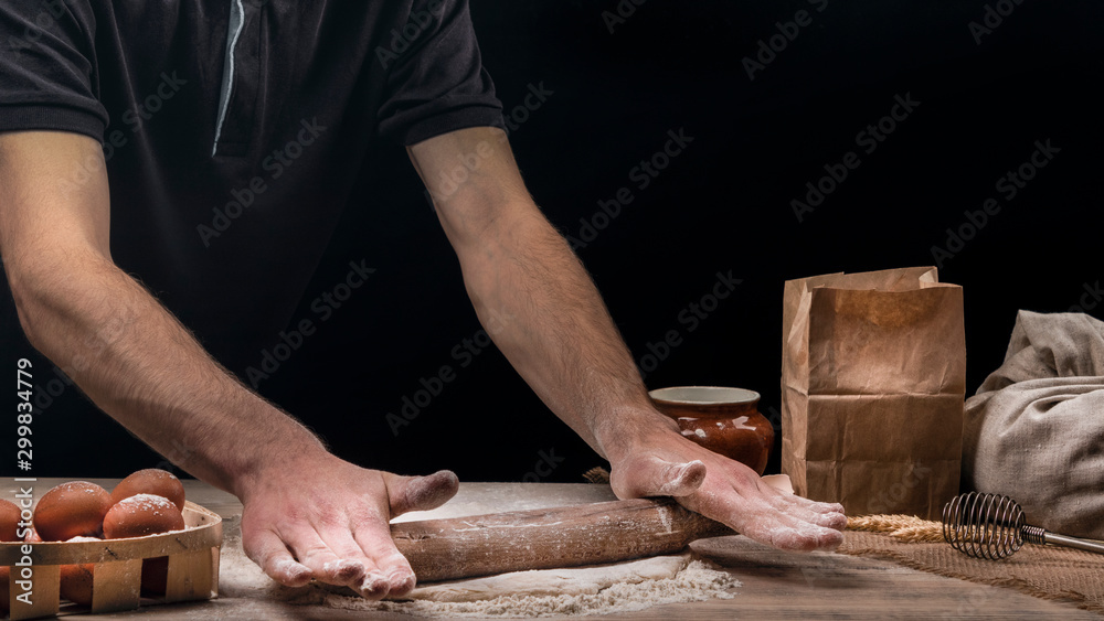 Baker is cooking bread. A man rolls out the dough