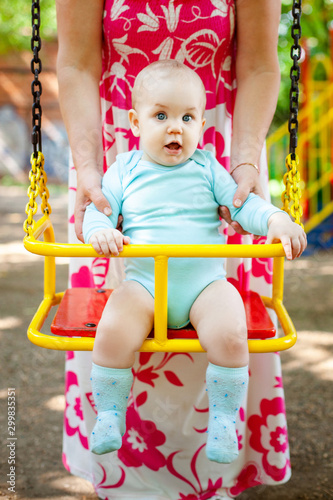 Child playing on outdoor playground. Little baby boy with parent plays on school or kindergarten yard. Active kid on colorful swing.
