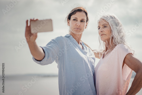 Mother and daughter spending a day at the sea, takinf¬¨‚Ä¢g smartphone selfies photo