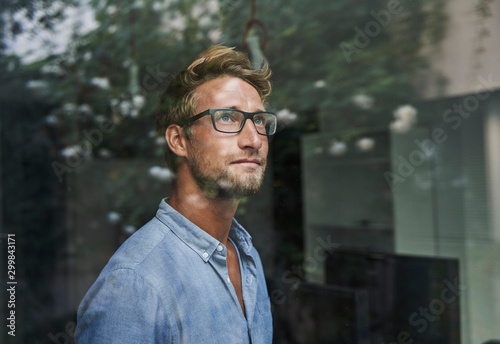 Casual young businessman behind windowpane in office