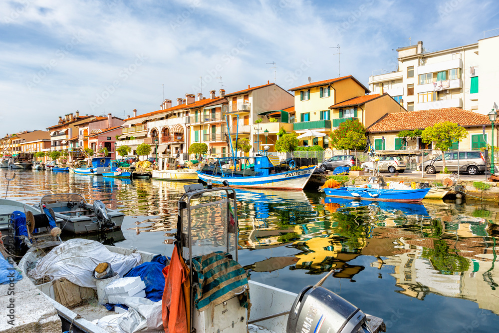 JULY 22, 2019 - GRADO, ITALY - Colored residential buildings and boats in the sunset light are mirror reflected in sea water of the old harbor of Grado, Northeastern Italy