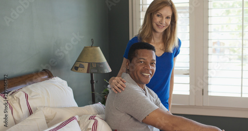 African American Man and Caucasian woman couple in bedroom smiling at camera