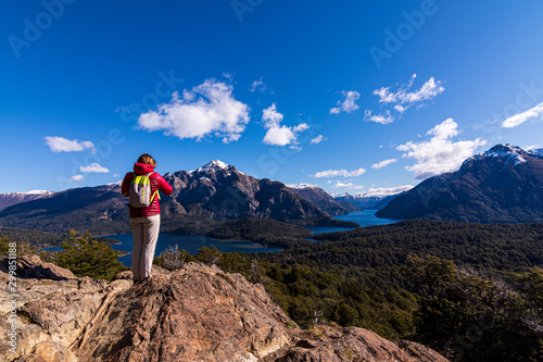 Rear view of female hiker wearing a backpach in the mountains against Andes range and Nahuel Huapi lake in Bariloche, Patagonia, Argentina