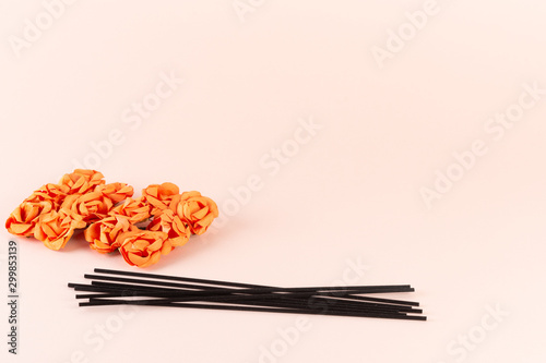 Black incense sticks with orange flowers on pink background