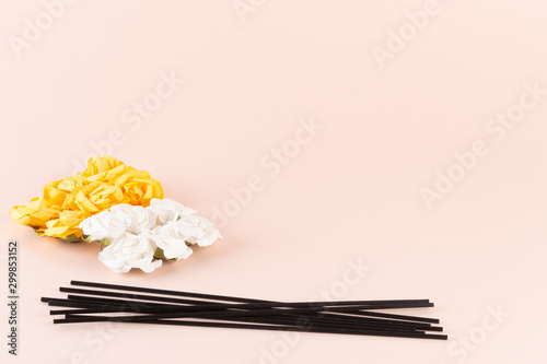 Black incense sticks with white and yellow flowers on pink background