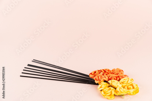 Incense sticks with orange and yellow flowers on pink background