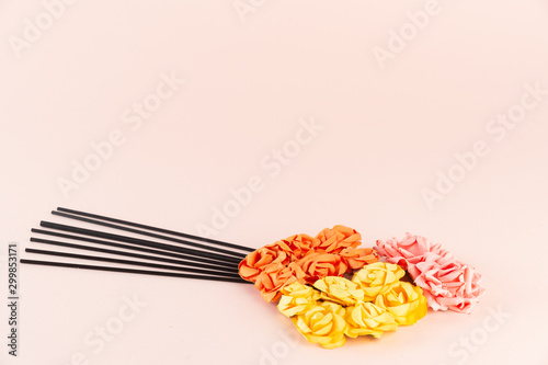 Incense sticks with pink, orange and yellow flowers on pink background