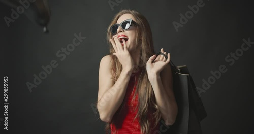 Pretty young woman posing to camera with black friday shopping bags and making surprise gesture, air balloons falling