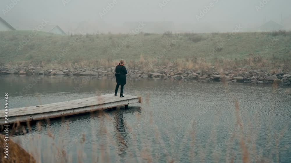 Woman stands alone on the edge of a jetty in cold weather Woman stands alone on the edge of a jetty in cold weather