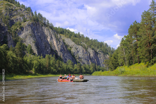 A group of people floating on the river in inflatable catamarans among the beautiful rocks and green coniferous forests with blue skies, Russia, Bashkortostan, the Belaya river Agidel.