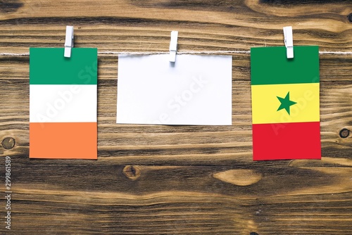 Hanging flags of Ireland and Senegal attached to rope with clothes pins with copy space on white note paper on wooden background.Diplomatic relations between countries.