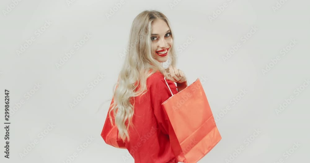 Happy pretty lady in red outfit holding shopping bags and goes fun in front of camera, glamorous lifestyle Happy pretty lady in red outfit holding shopping bags and goes fun in front of camera, glamorous lifestyle