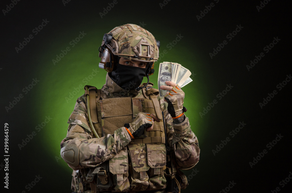 Fototapeta premium a male soldier in military clothes with a weapon on a dark background with money
