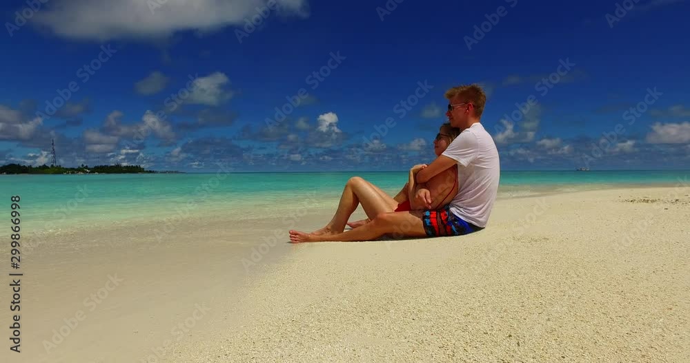Young couple sitting on the beach while hugging with clear blue sky background in Canada- Steady Shot Young couple sitting on the beach while hugging with clear blue sky background in Canada- Steady Shot