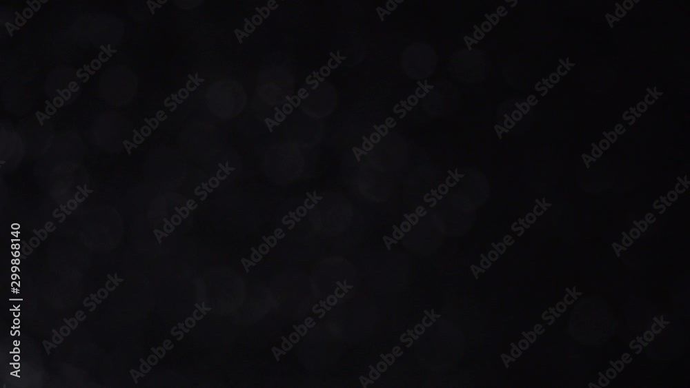 Seamlessly looping subtle slowly rotating dark silver bokeh particles on black background.