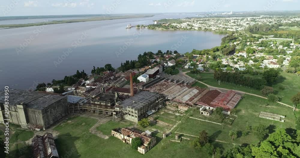 Aerial general view of old abandoned factory at riverbend. Backgorund of Fray Bentos city. To general top view of construction. Unesco, The Anglo, Uruguay Aerial general view of old abandoned factory at riverbend. Backgorund of Fray Bentos city. To general top view of construction. Unesco, The Anglo, Uruguay