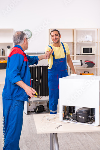 Two contractors repairing fridge at workshop