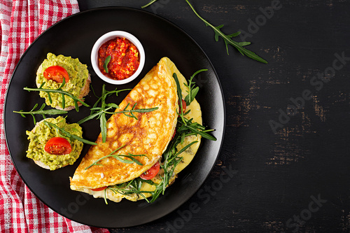Breakfast. Omelette with tomatoes, cheese, green arugula and toasts with avocado cream on black plate. Frittata - italian omelet. Top view
