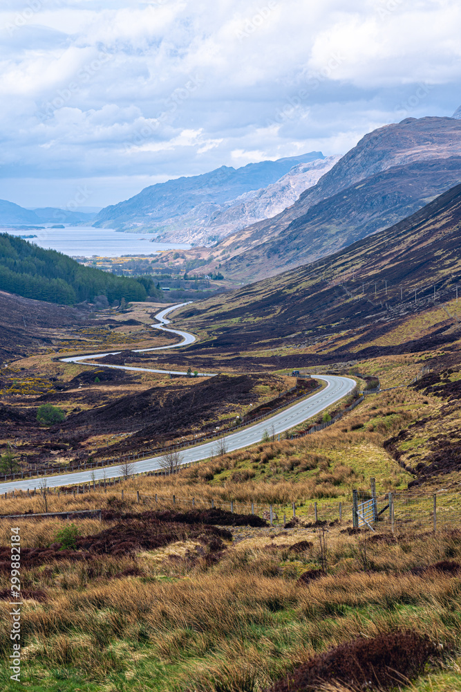 Glencoe in the Highlands of Scotland, scene of the historic 1692 massacre. The old road meanders between rocky mountain slopes across moorland covered with wild flowers and purple heather.