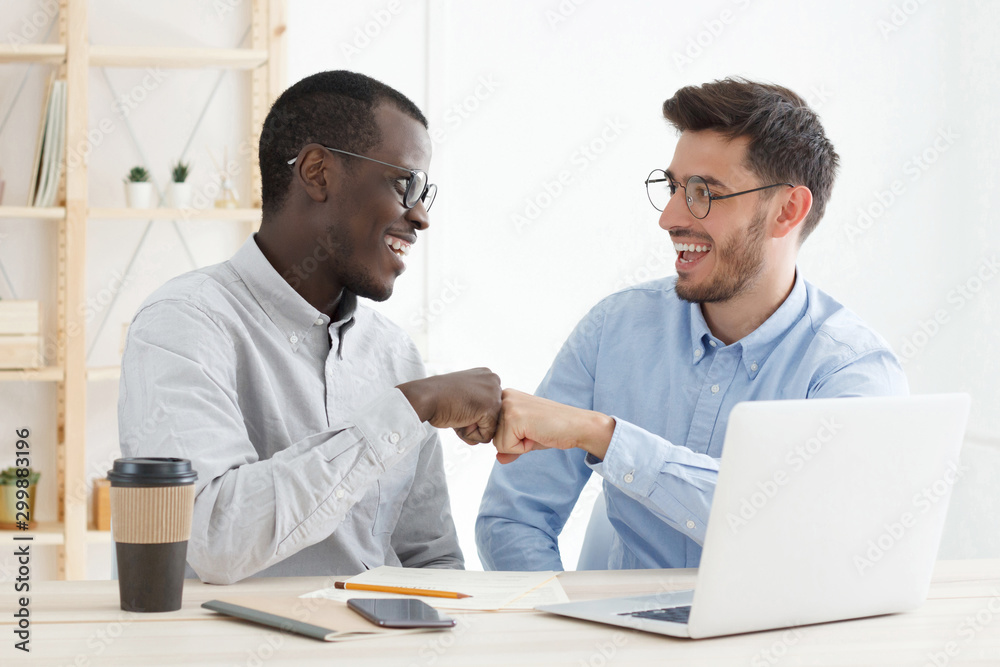 Happy african and european men working in office, bumping fists after having agreed on common multiethnic project Happy african and european men working in office, bumping fists after having agreed on common multiethnic project