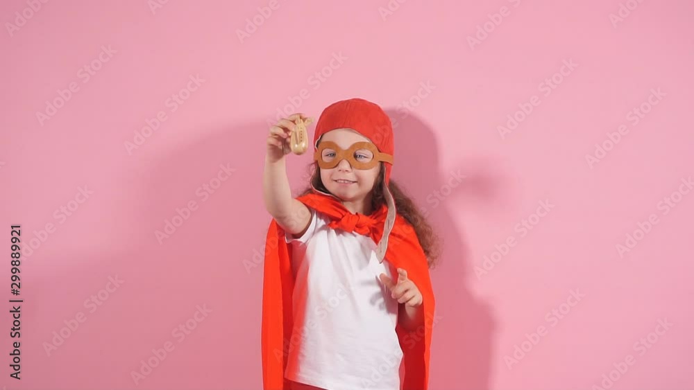 Awesome girl child wearing red cloak and helmet of pilot raised hands up holding wooden toy plane. Imagination of pilot, aviation concept Awesome girl child wearing red cloak and helmet of pilot raised hands up holding wooden toy plane. Imagination of pilot, aviation concept