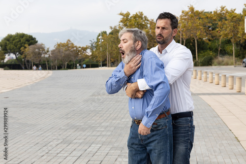 Man doing the Heimlich maneuver to an old man with suffocation due to obstruction of the airway with food photo