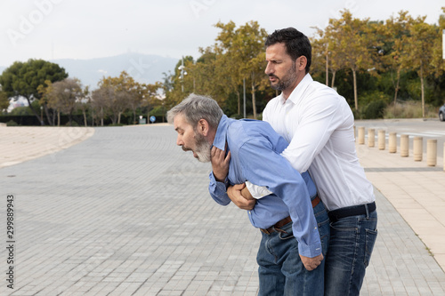 Man doing the Heimlich maneuver to an old man with suffocation due to obstruction of the airway with food photo