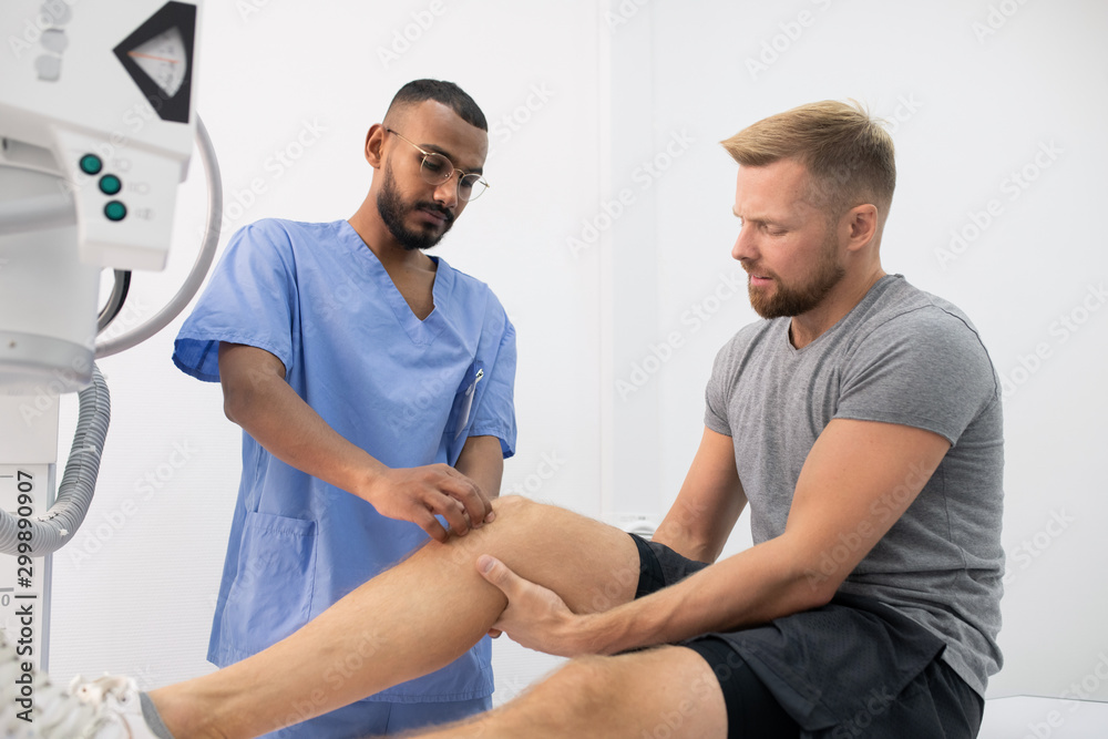 Obraz premium Young doctor in uniform massaging sick knee of one of patients in hospital