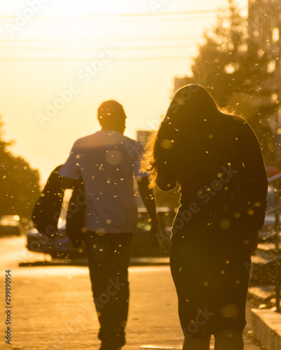 Silhouette of a young girl in a dress that walks around the city in the sun light during sunset. Golden rays of the sun. Back view.