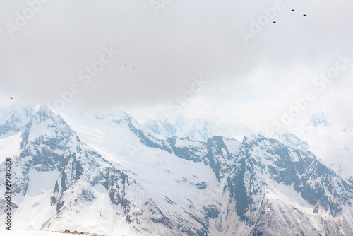 mountain peaks and slopes covered with snow, winter in the Caucasus mountains, birds in the sky, clouds,