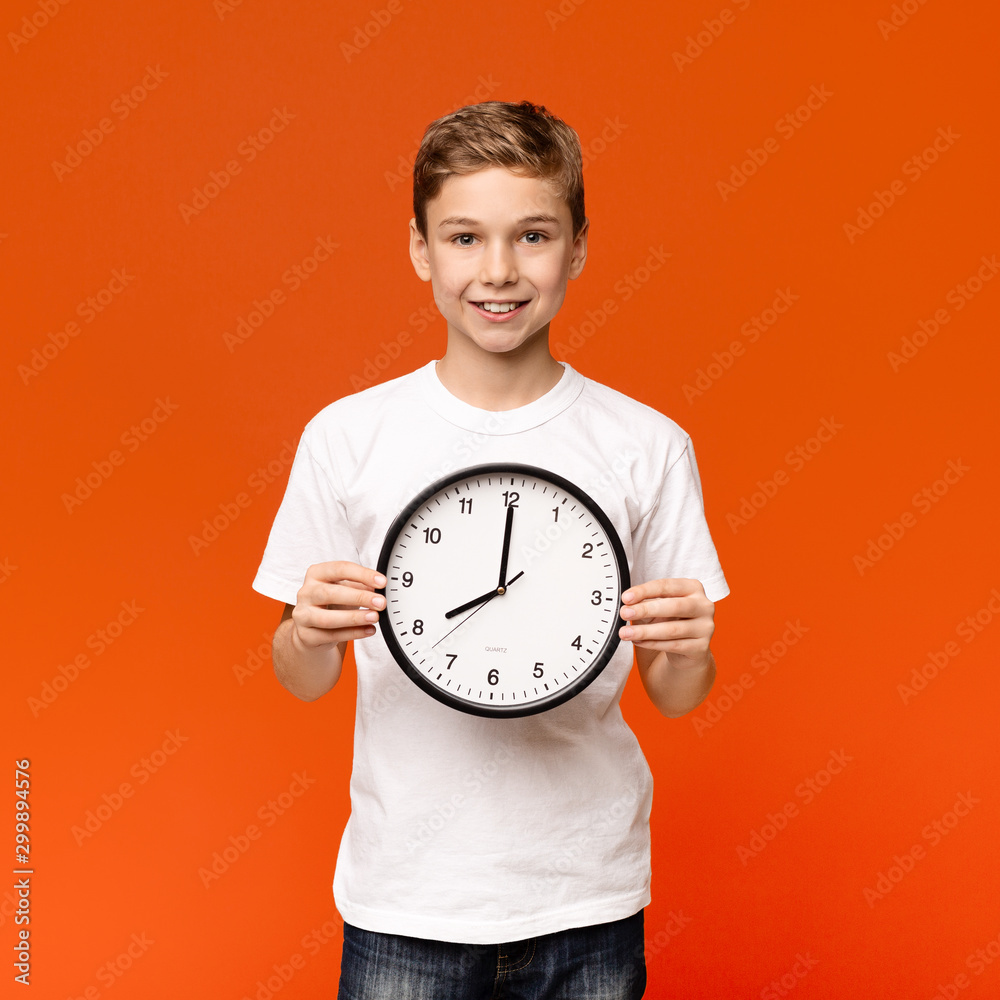 Smiling teen boy holding big clock, orange background Smiling teen boy holding big clock, orange background
