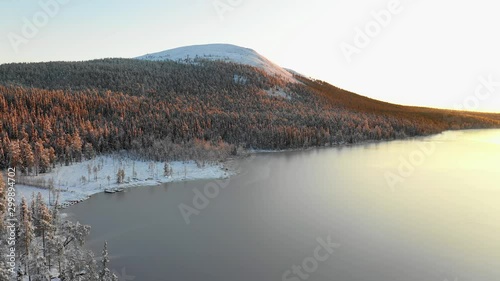 Aerial, descending, drone shot, of snowy, Kesankitunturi fell, frozen Kesankijarvi lake and first snow on trees, sunset, on a sunny, autumn evening, in Pallas-Yllas national park, in Lapland, Finland photo