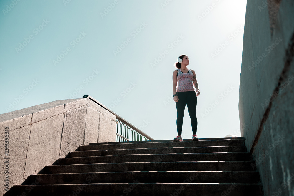 Sporty lady in headphones standing on top of the stairs